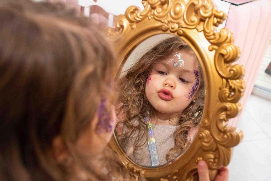 Niña maquillada con glitter mirándose al espejo durante su cumpleaños.
