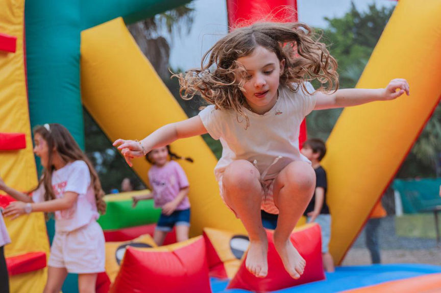 Niña saltando feliz en castillo inflable durante un cumpleaños infantil al aire libre.