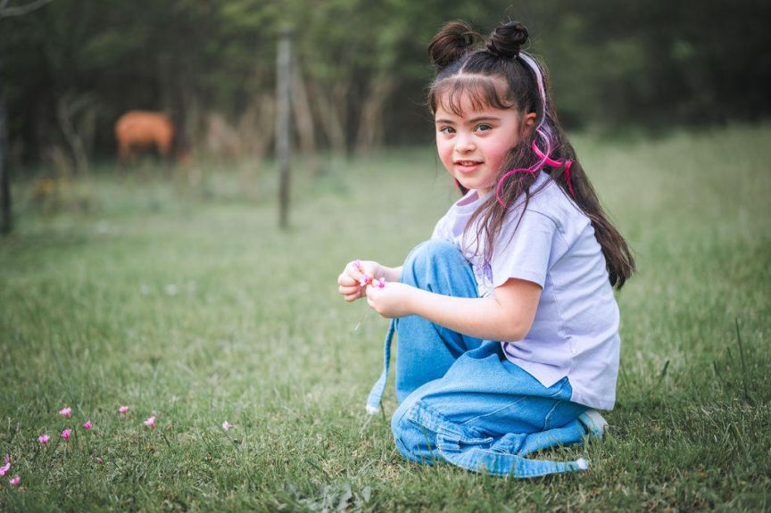 Retrato de niña sonriente sentada en el pasto recogiendo flores durante su cumpleaños.