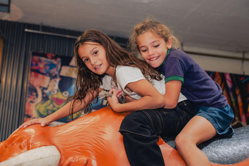 Dos niñas riendo mientras montan un toro mecánico en una fiesta infantil.