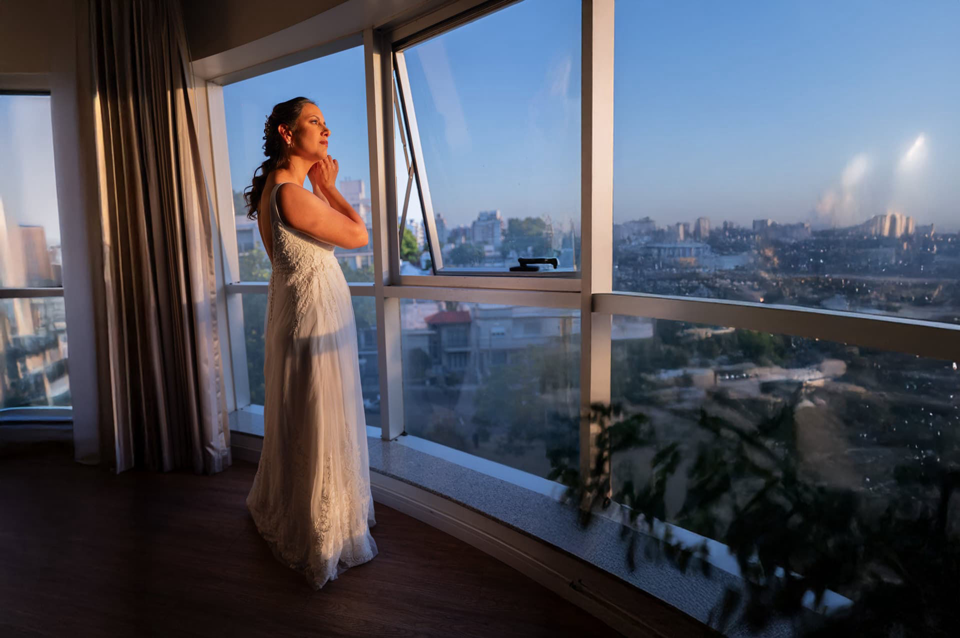 Novia en su preparación mirando por la ventana al atardecer en Montevideo antes de su casamiento.
